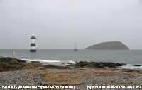 Under grey skies and rain a ketch leaves the Menai Strait through Puffin Sound at high water.